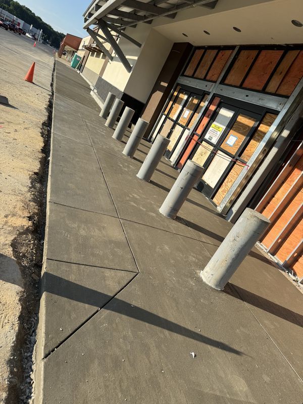 Tilted view of a store entrance sidewalk with concrete bollards and orange cones in front of glass doors