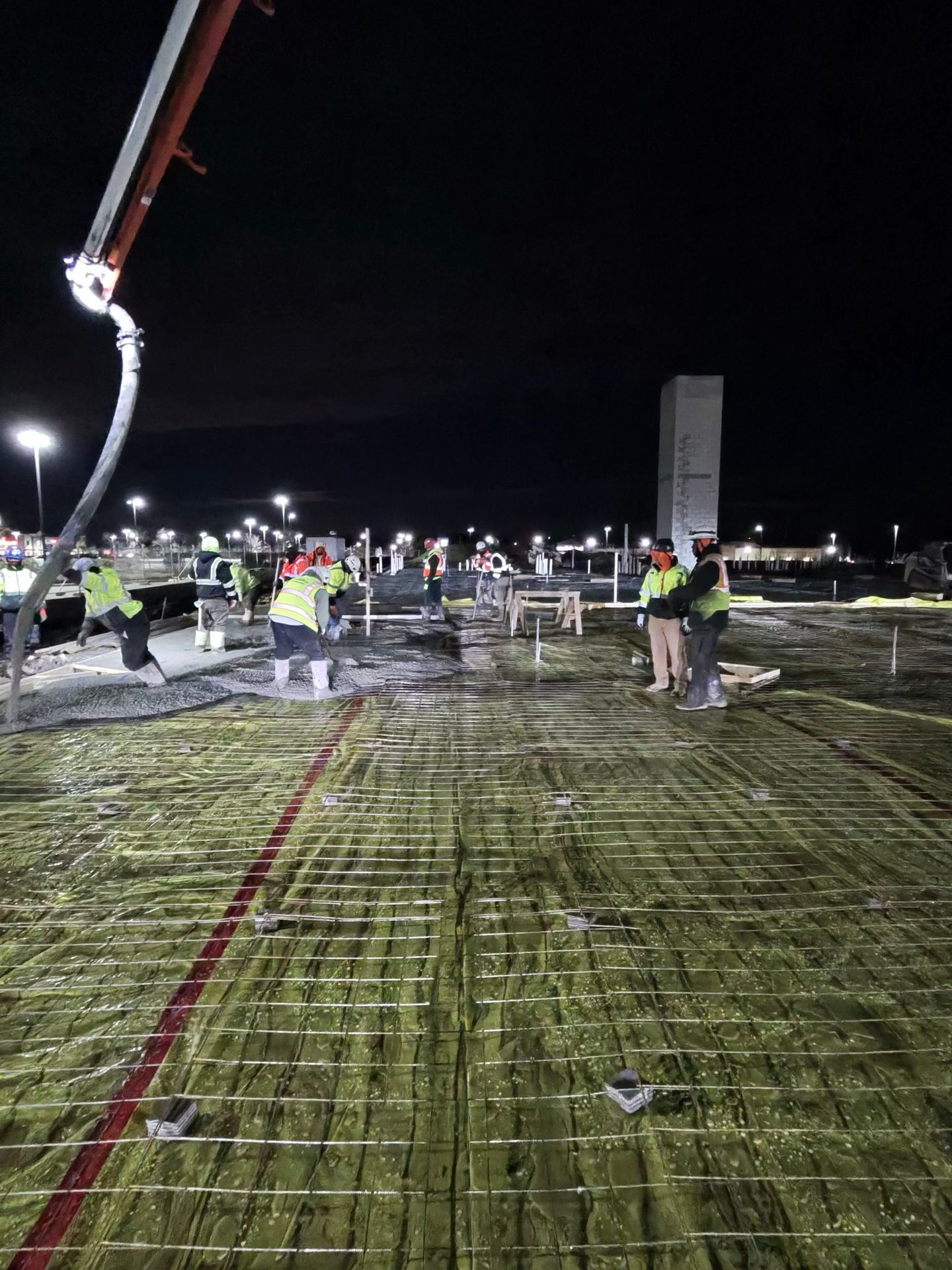 Night construction site with workers in safety vests on rebar-covered ground under bright lights