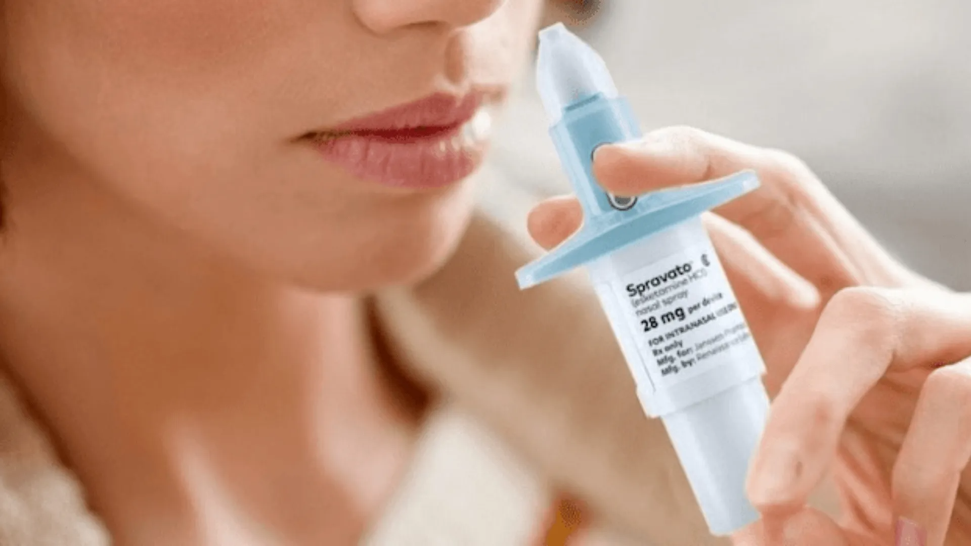 Person holding a nasal spray dispenser near their nose, preparing to use it