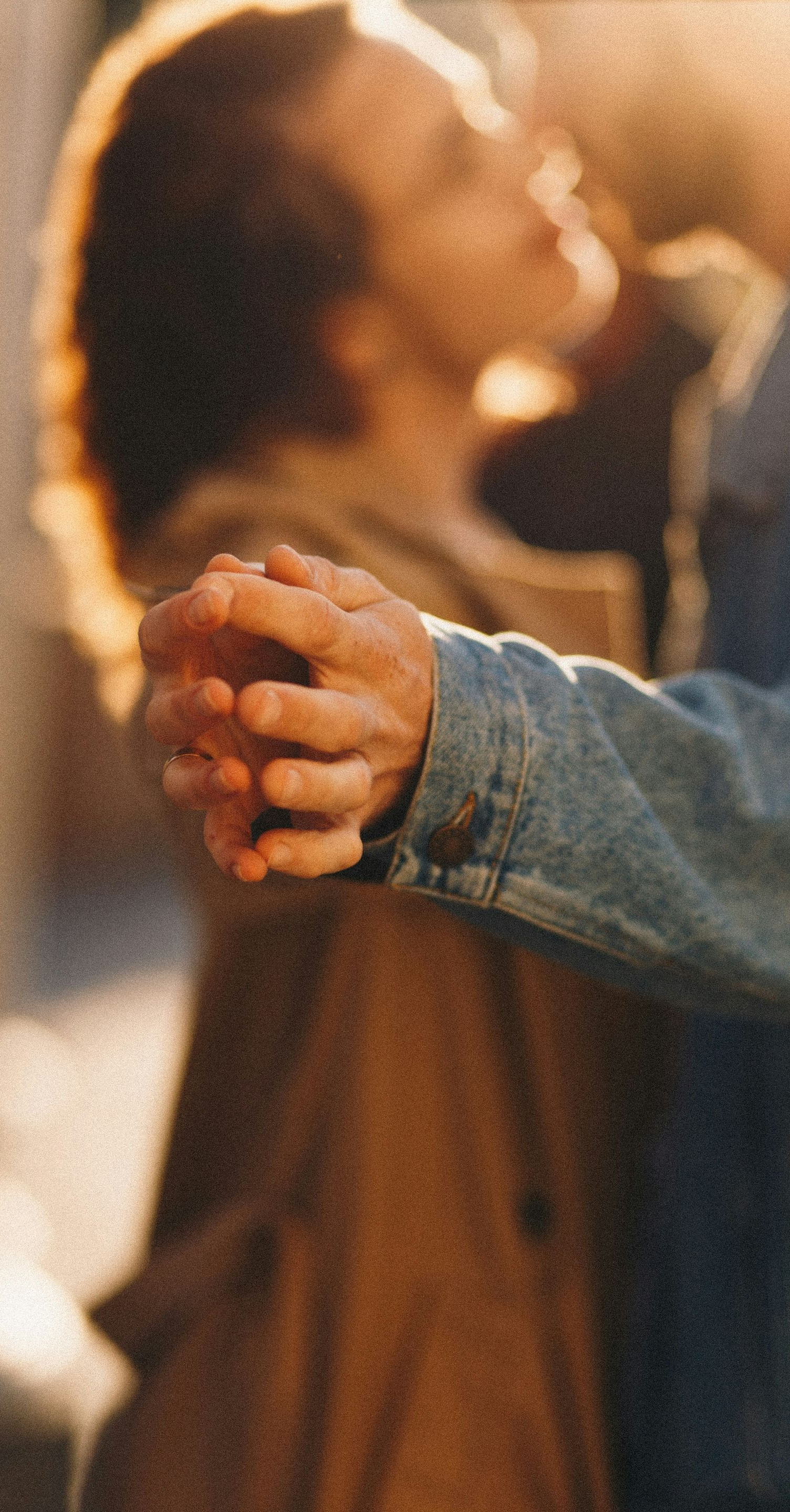 Hands clasped in a warm, blurred portrait with soft golden light