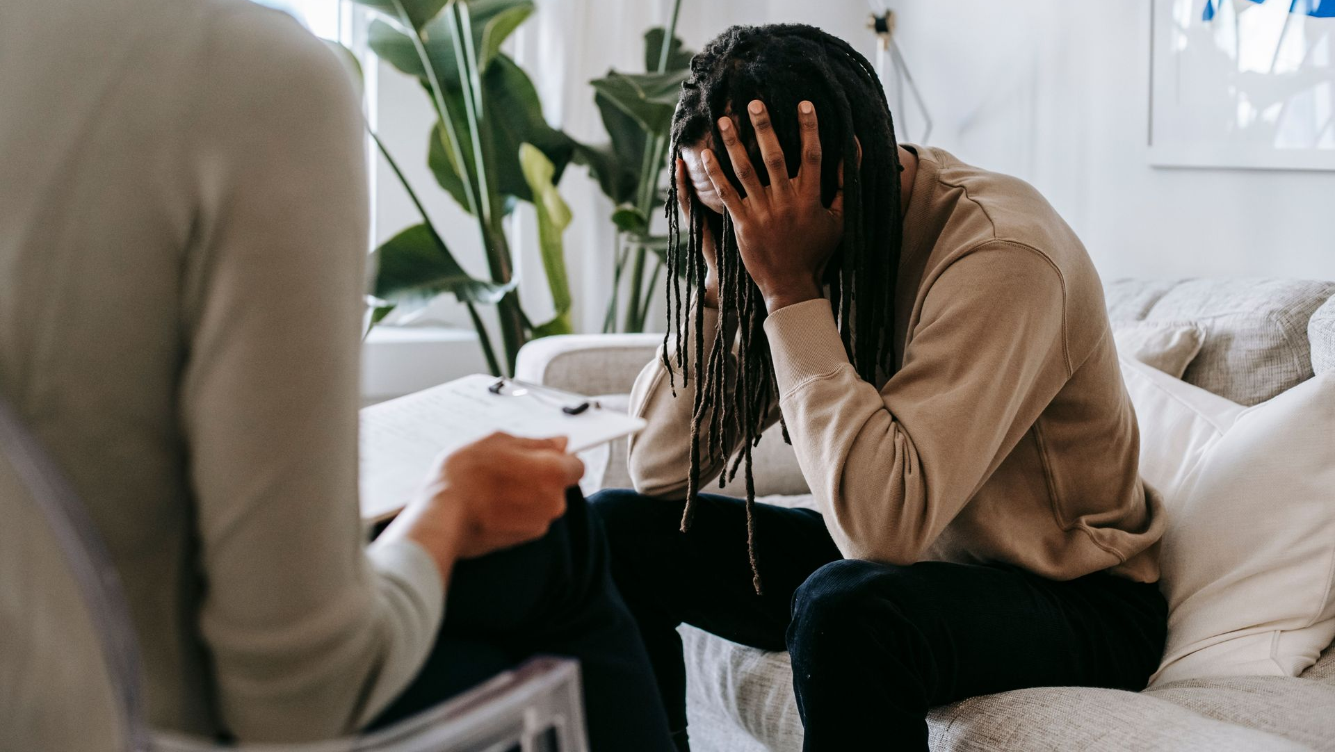 Person sits on a couch with head in hands during a counseling session.