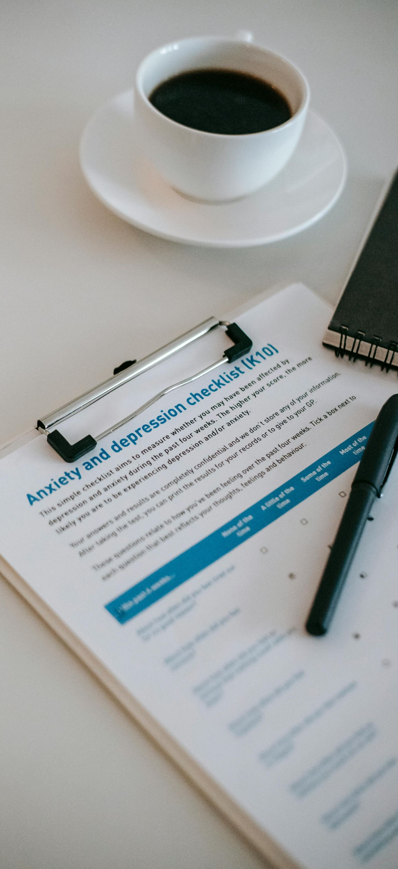 Coffee cup beside clipboard with documents, pen, and notebook on a desk