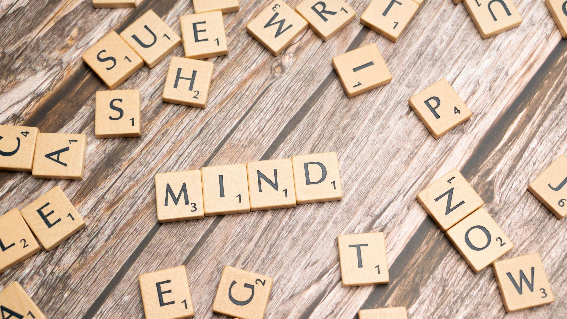 Wooden letter tiles spelling “MIND” on a rustic table, with scattered letters around them.