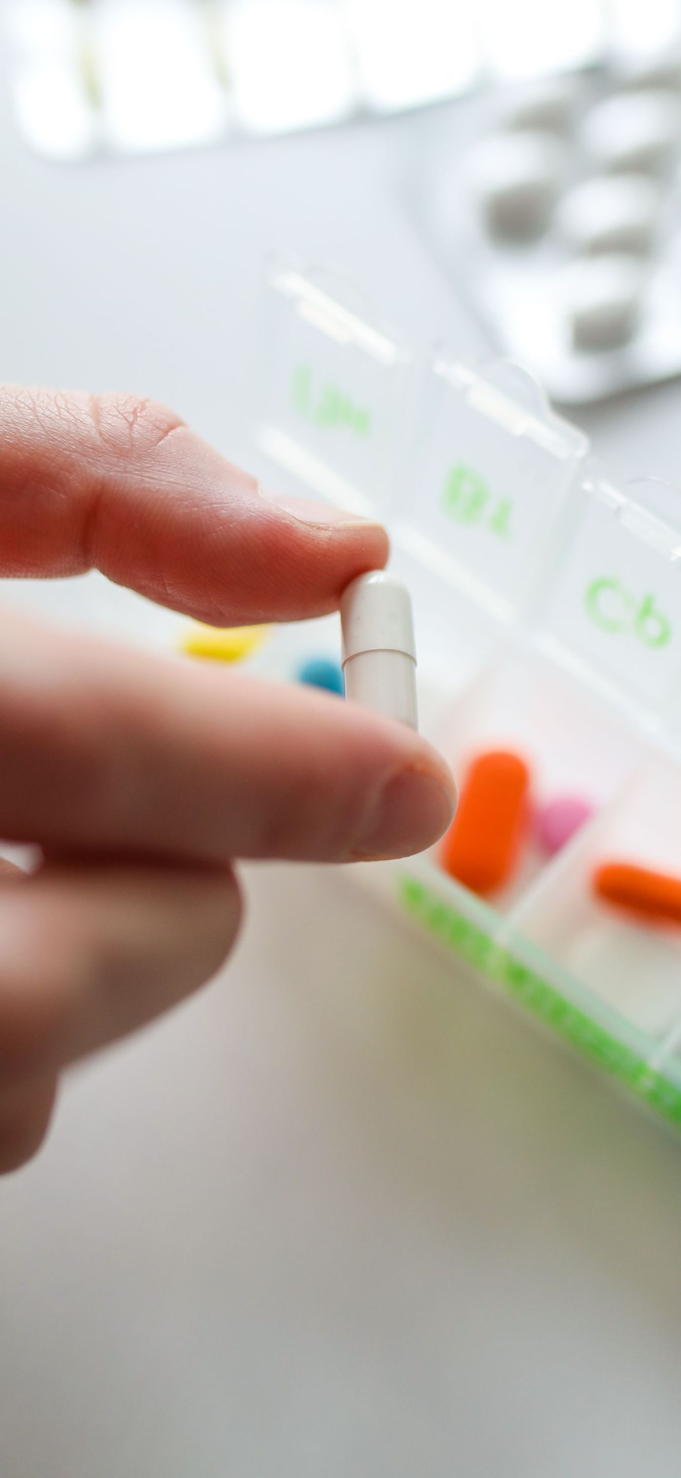 Hand placing a capsule into a pill organizer with orange and clear medication capsules