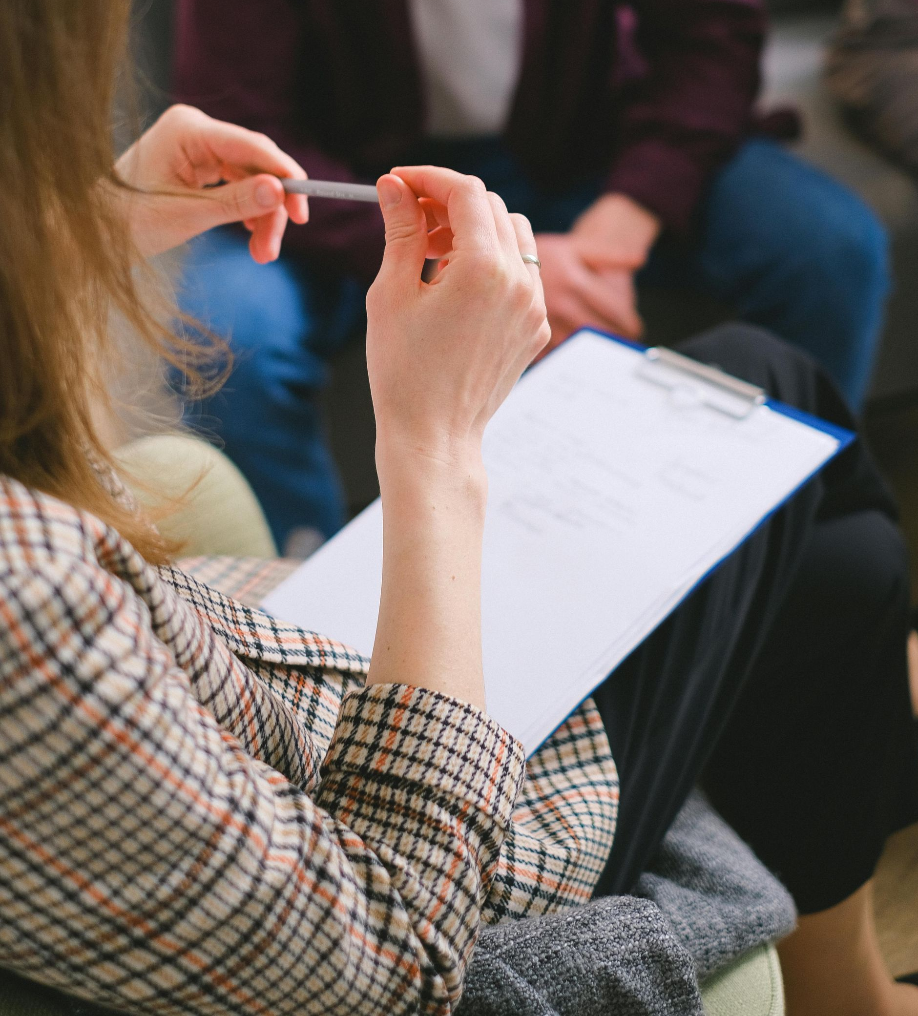 People in a group discussion, one taking notes on a clipboard and holding a pen.