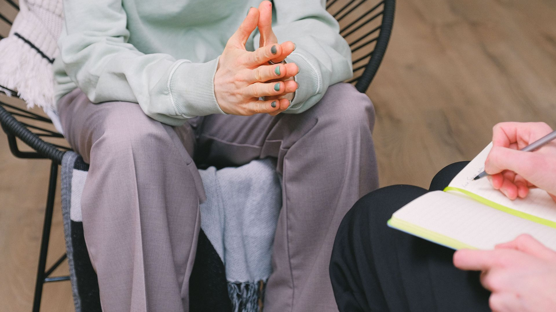 Two people seated in discussion, one taking notes in a notebook.