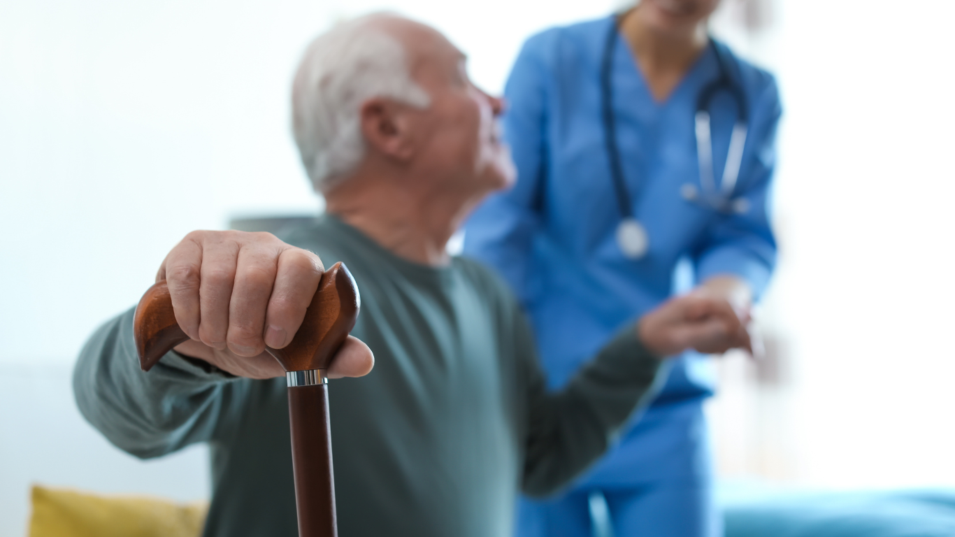 An elderly man with a cane is standing next to a nurse.