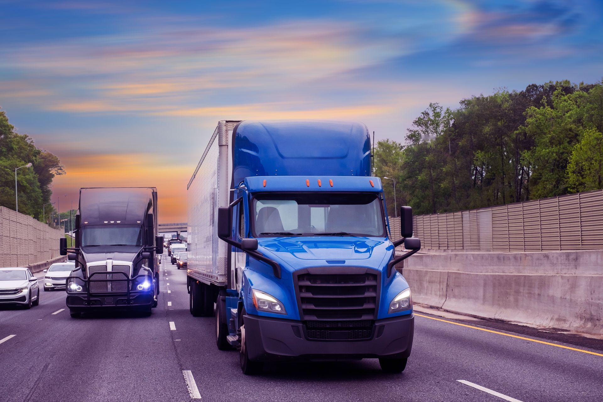 Two semi trucks are driving down a highway at sunset.