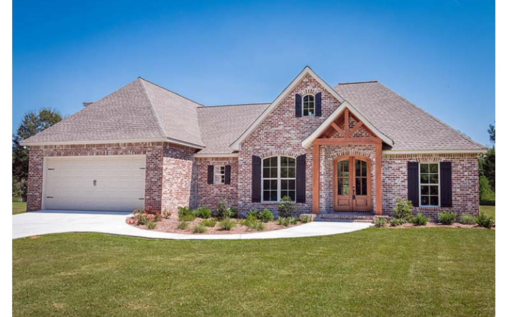 A large brick house with a large garage and a lush green lawn in front of it.
