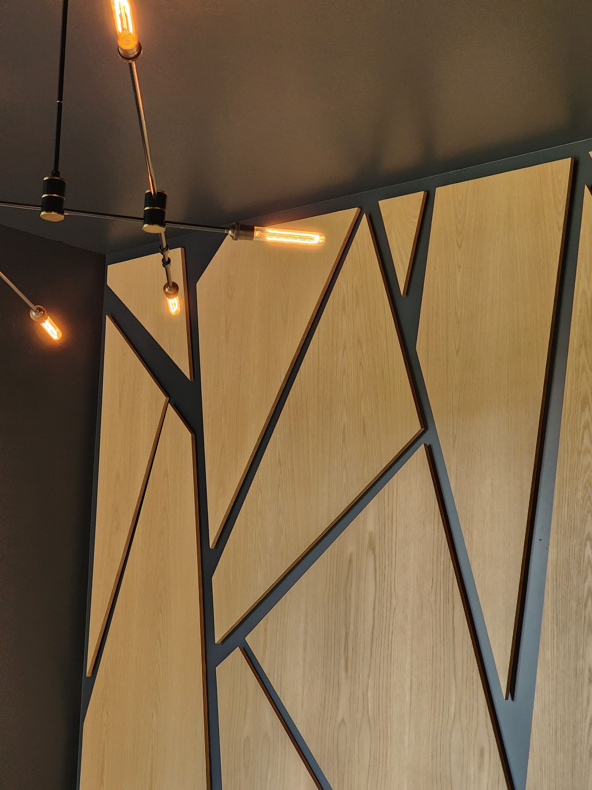 A wooden wall with a geometric design and lights hanging from the ceiling