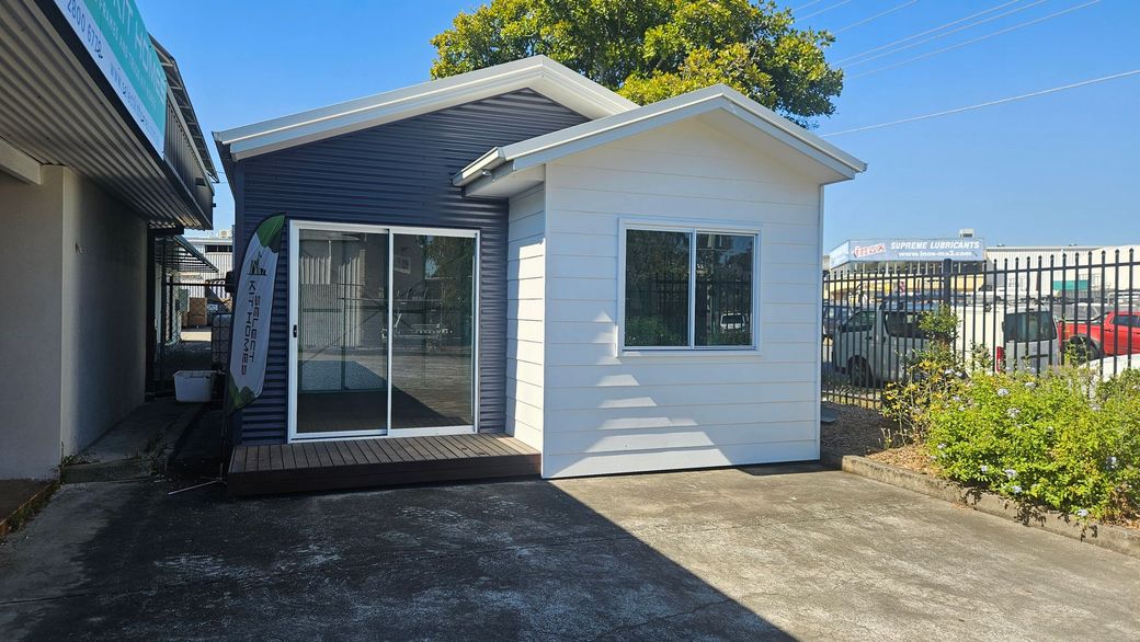 Small building with blue and white siding, sliding glass doors, and a window, outside.