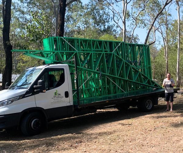 Green framed building on truck, man next to it outdoors.