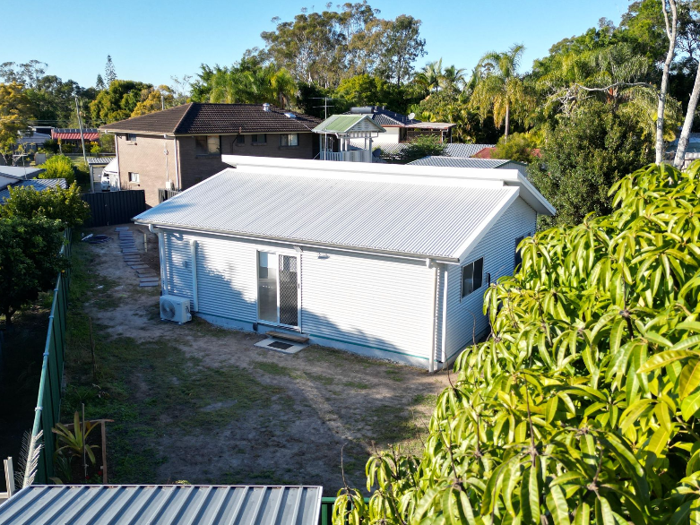 White house with a silver roof, backyard with trees and other houses in the background.