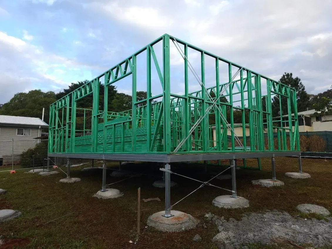 Green wooden house frame under construction on concrete piers outdoors.