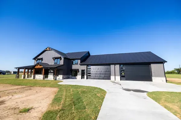 Modern farmhouse with black roof and garage, set on a sunny lot with a curved concrete driveway.