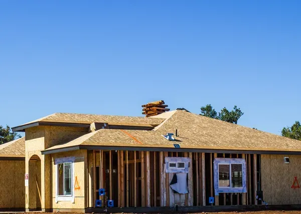 Partially built house with exposed framing and a tan roof under a clear blue sky