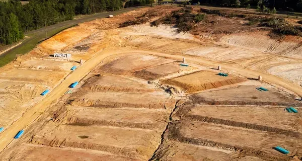 Aerial view of a large dirt construction site with graded earth and blue pipes or markers.