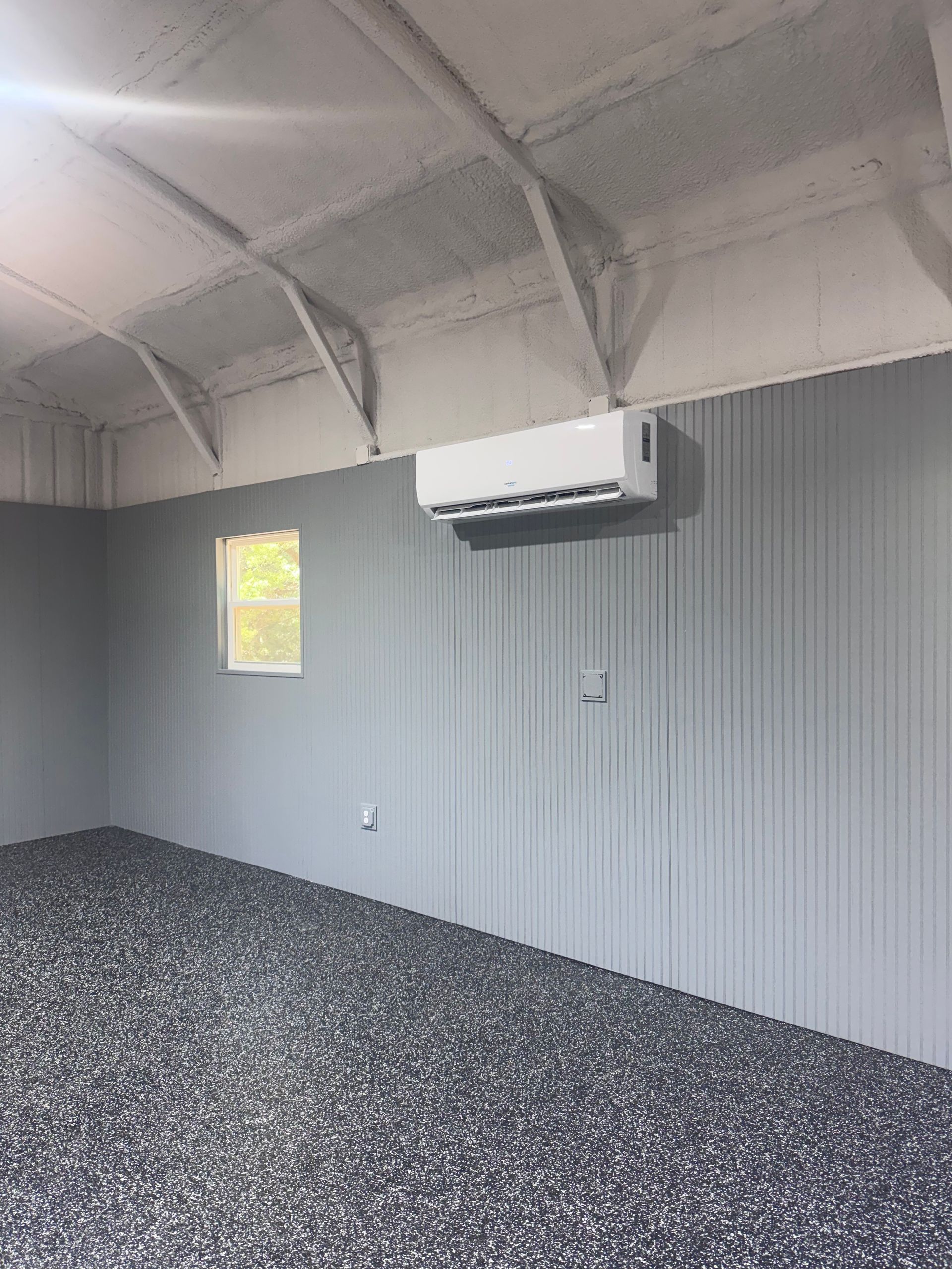 Empty room with gray paneled walls, patterned floor, and a wall-mounted air conditioner on a vaulted ceiling.