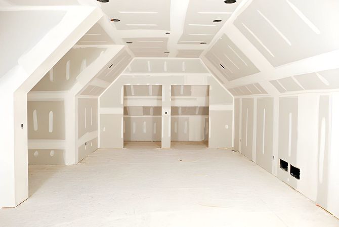 Empty unfinished white room with sloped ceiling and exposed drywall, likely under construction