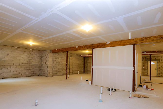 Empty unfinished room with exposed brick walls, drywall panels, and ceiling lights under construction