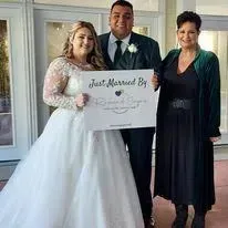 Newlyweds with officiant holding a “Just Married” sign outside a venue