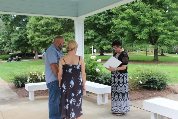 Three people stand under a pavilion; one reads from a paper in a park.