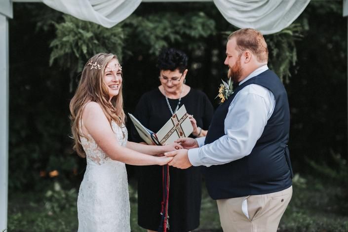 Wedding couple holding hands during outdoor ceremony beneath white drapery, officiant standing behind them.