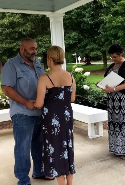 Two people talk under a gazebo while another person holds papers nearby outdoors.
