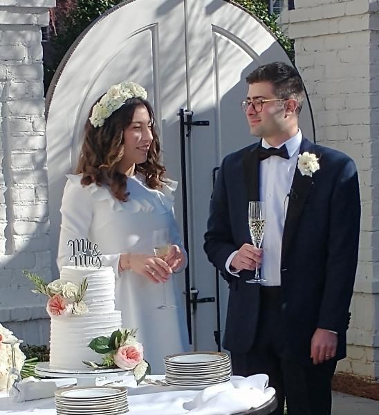 Bride and groom in formal wear with champagne glasses at an outdoor wedding reception table