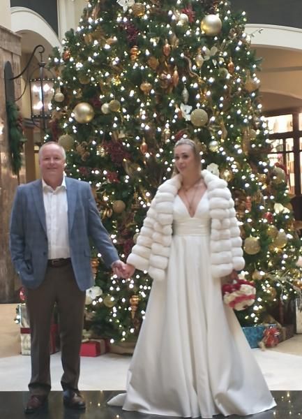 Couple holding hands in front of a large decorated Christmas tree in a lobby