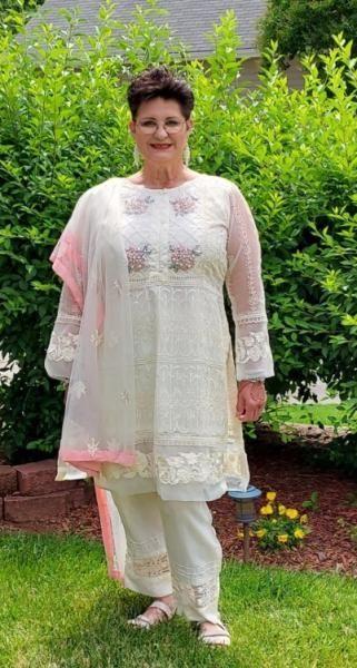 Woman in a light pink embroidered outfit standing on a lawn in a garden.