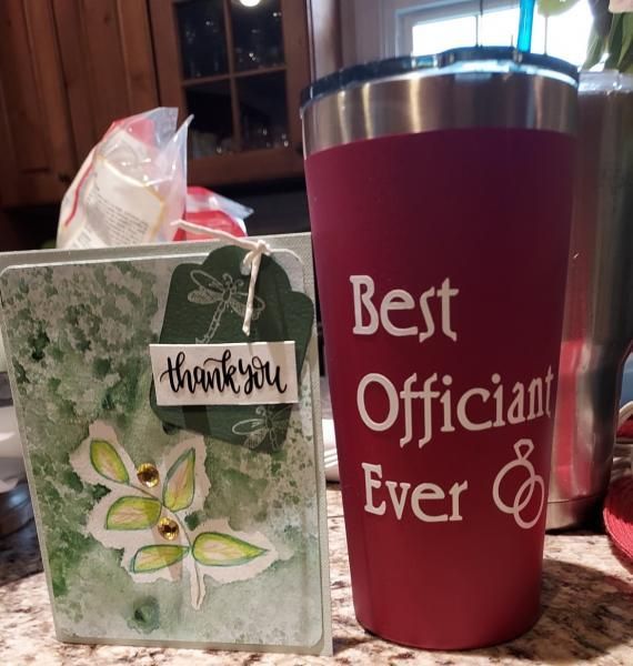 Thank-you gift bag and maroon tumbler reading “Best Officiant Ever” on a kitchen counter