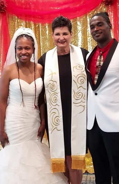 Three people posing at a wedding altar, with red drapes and white-and-gold decor behind them