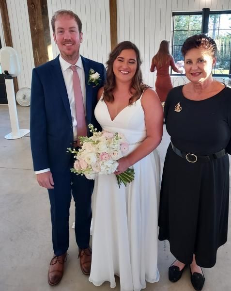 Three people posing indoors at a wedding, with the bride holding a bouquet and smiling.