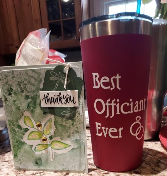 Thank-you card beside red tumbler reading “Best Officiant Ever” on a kitchen counter