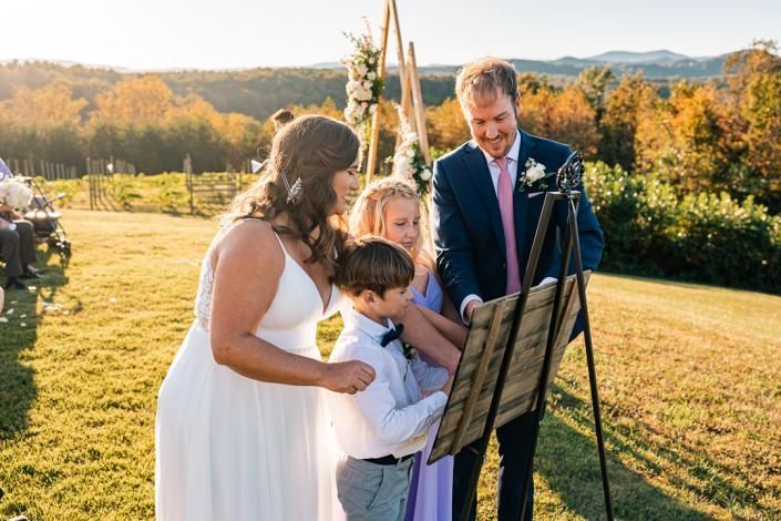 Wedding party reading from a music stand outdoors at sunset in a grassy field, with mountains in the background