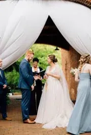Bride and groom exchanging vows under white drapes at an outdoor wedding ceremony