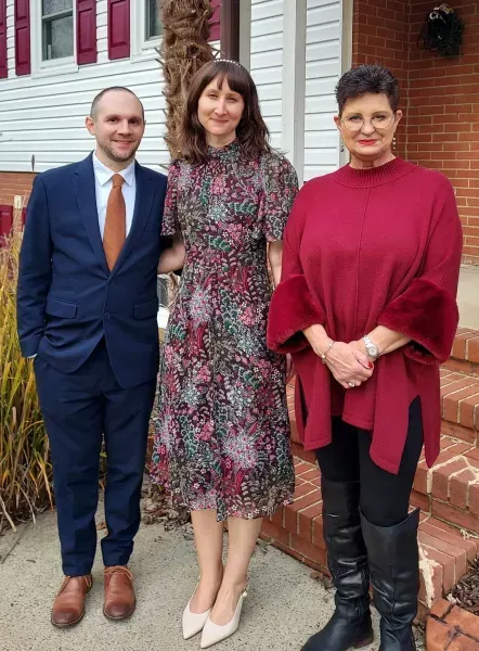 Three people standing outside a brick building, dressed in formal attire