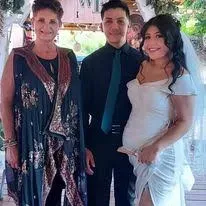 Three people posing at a wedding, with a bride in a white dress and veil beside two guests in formal attire