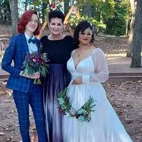 Three people posing outdoors in formal attire, holding bouquets at a wedding ceremony