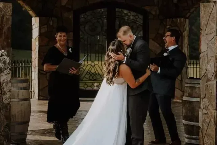 Wedding couple kissing beside an officiant and best man under a stone archway