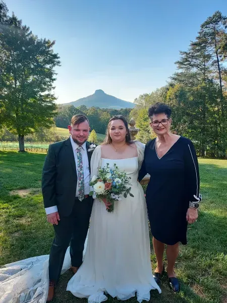 Wedding couple posing with an older woman outdoors, with a mountain in the background.