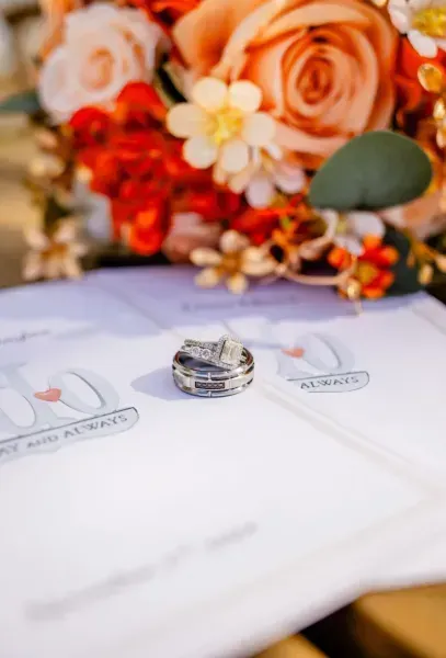 Wedding rings on a white card with peach roses and flowers in the background