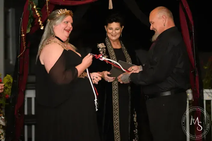 Three people on a stage during a ribbon-cutting ceremony, holding red-and-white ribbon and scissors.
