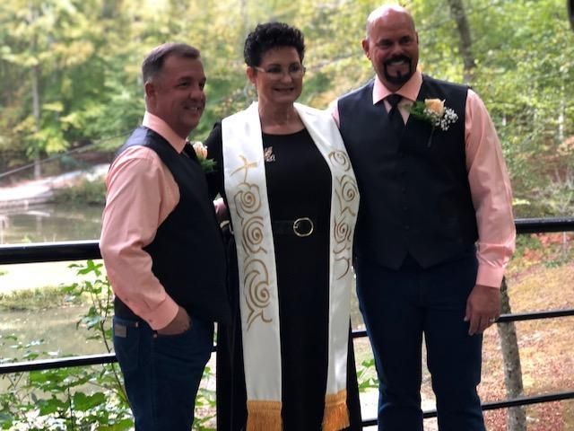 Three people posing together outdoors by a railing in front of a wooded stream.
