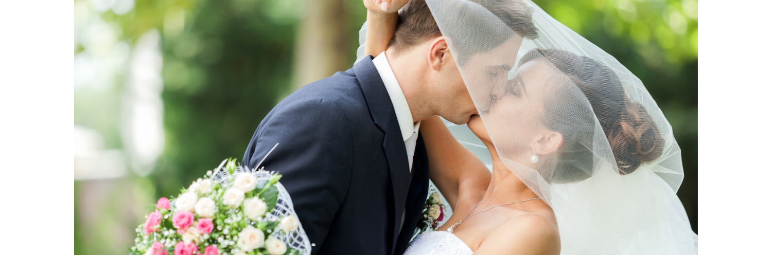 Bride and groom kissing outdoors, with a bouquet in the foreground