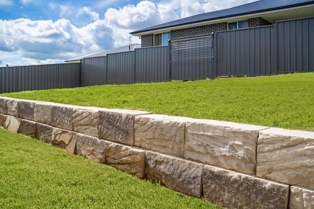 A Stone Wall Surrounds A Lush Green Lawn In Front Of A House — Central West Budget Tree Services in Dubbo, NSW