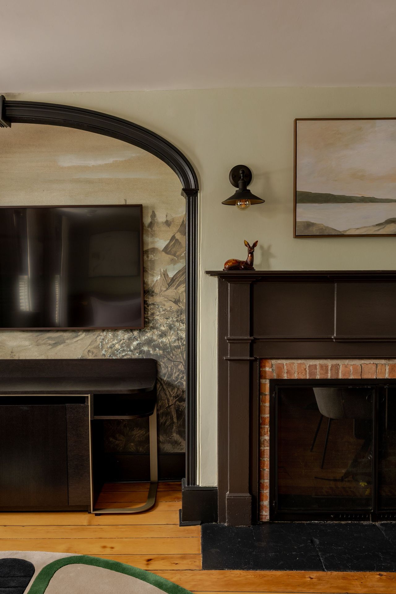 A living area with a fireplace, dark wooden mantel, arched black metal structure, TV, and neutral-toned wall art.