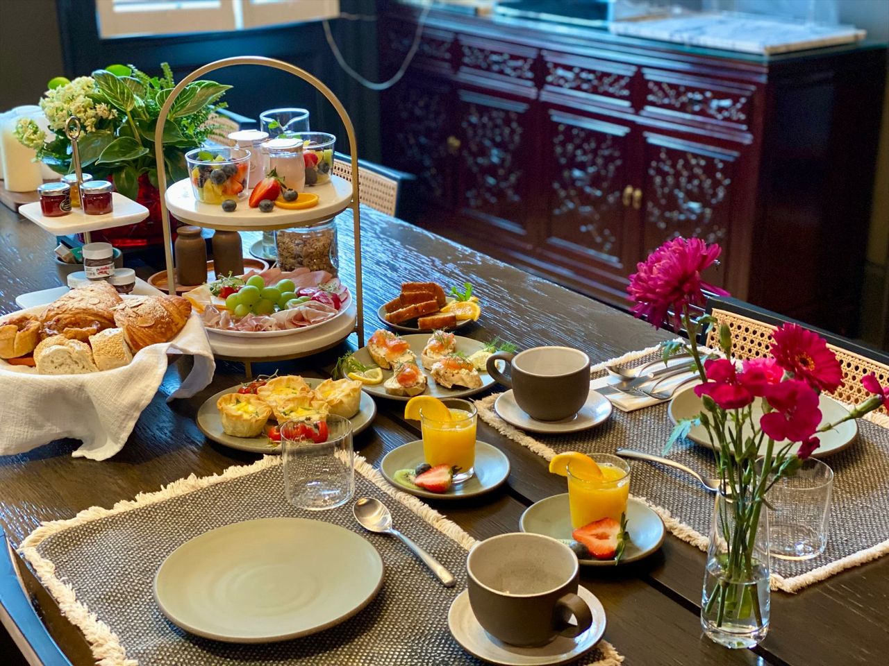 Elegant tea table with pastries, sandwiches, cups, and pink flowers by a window