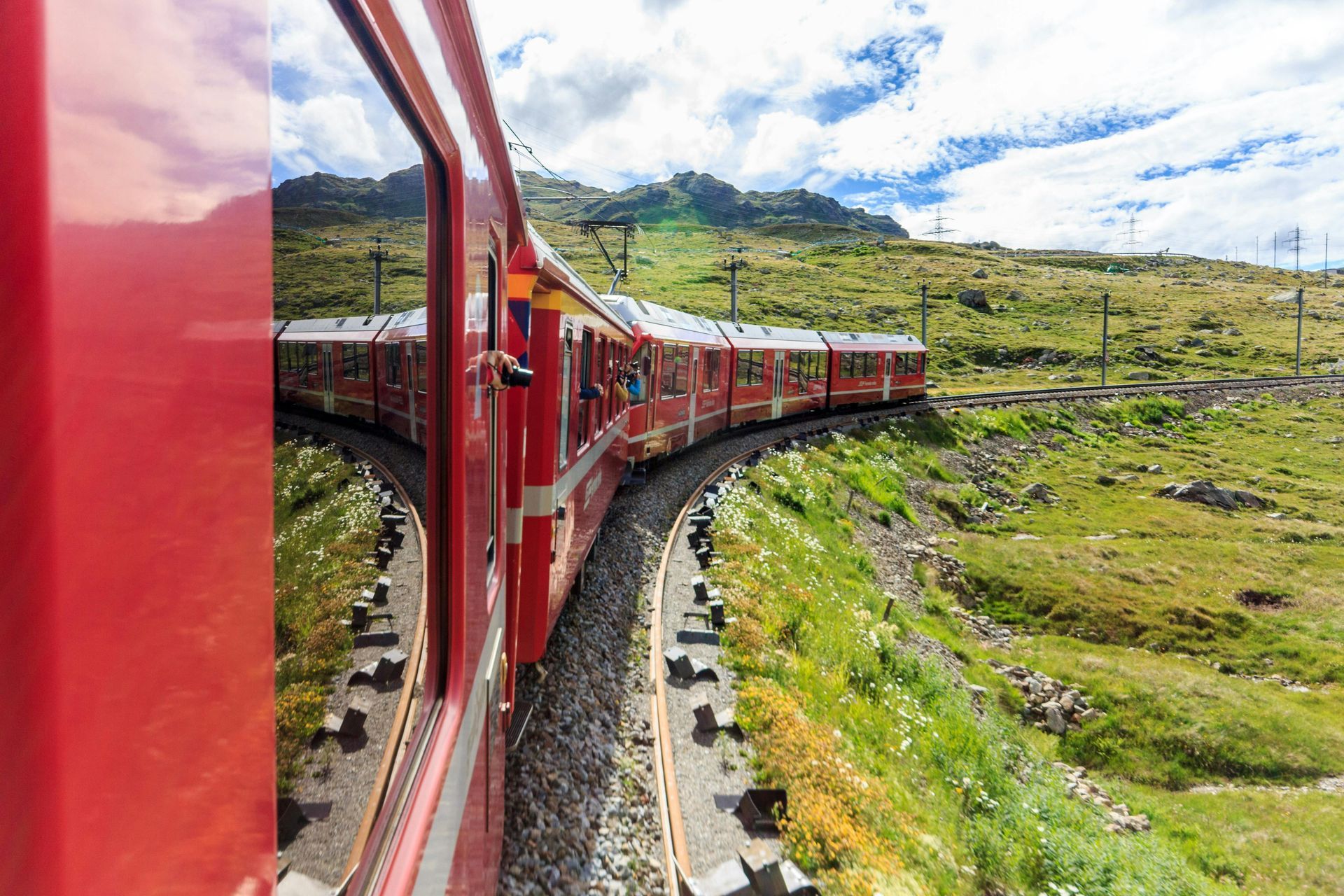 photo taken from the window of a red train traveling through a green landscape in Switzerland